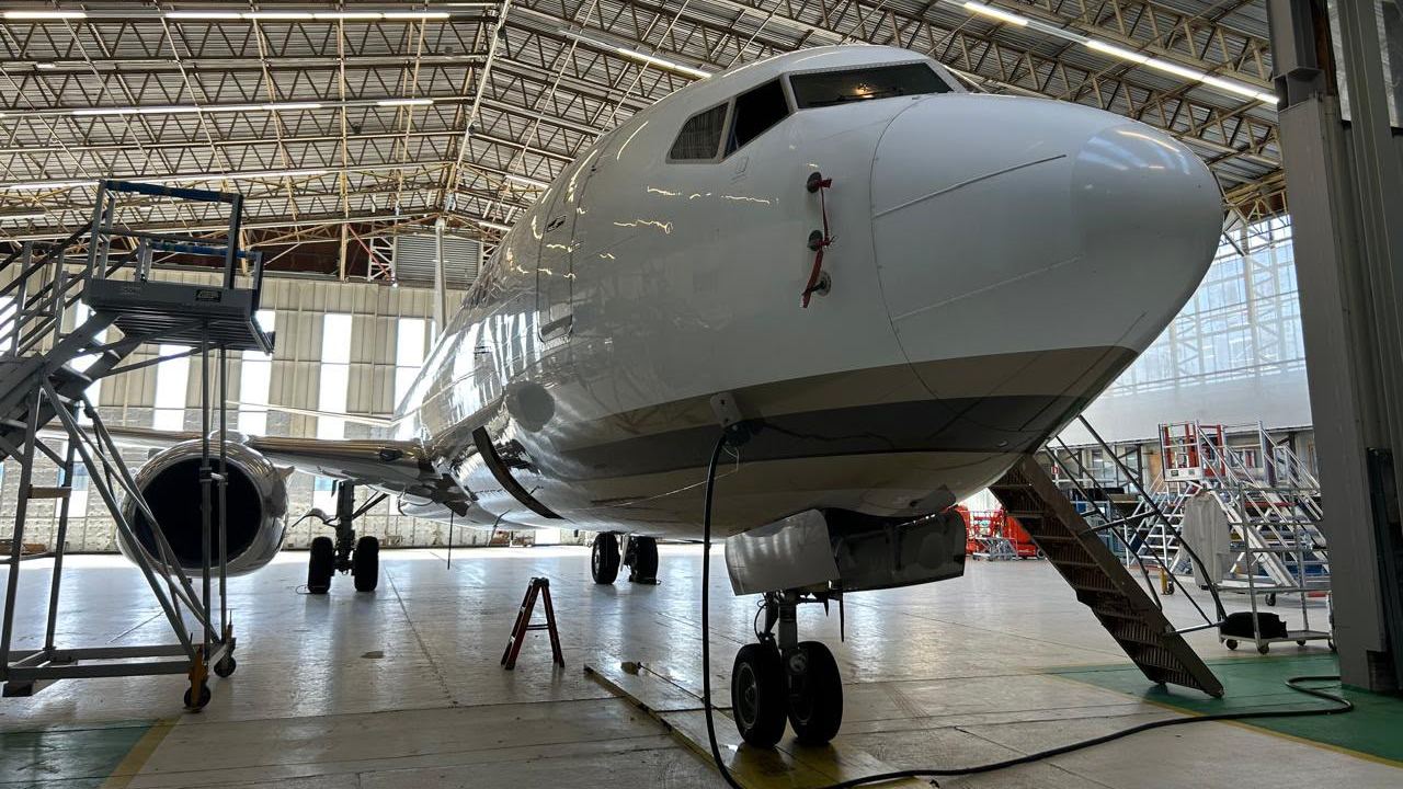 A white Boeing 737-family business jet in a large hangar, with covers and red remove-before-flight streamers.